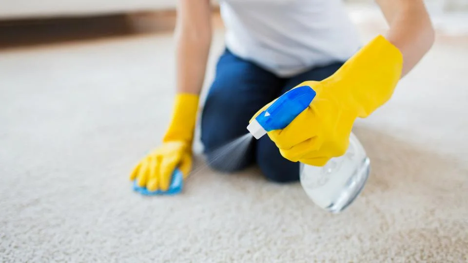 a person wearing yellow gloves spraying a spray on carpet